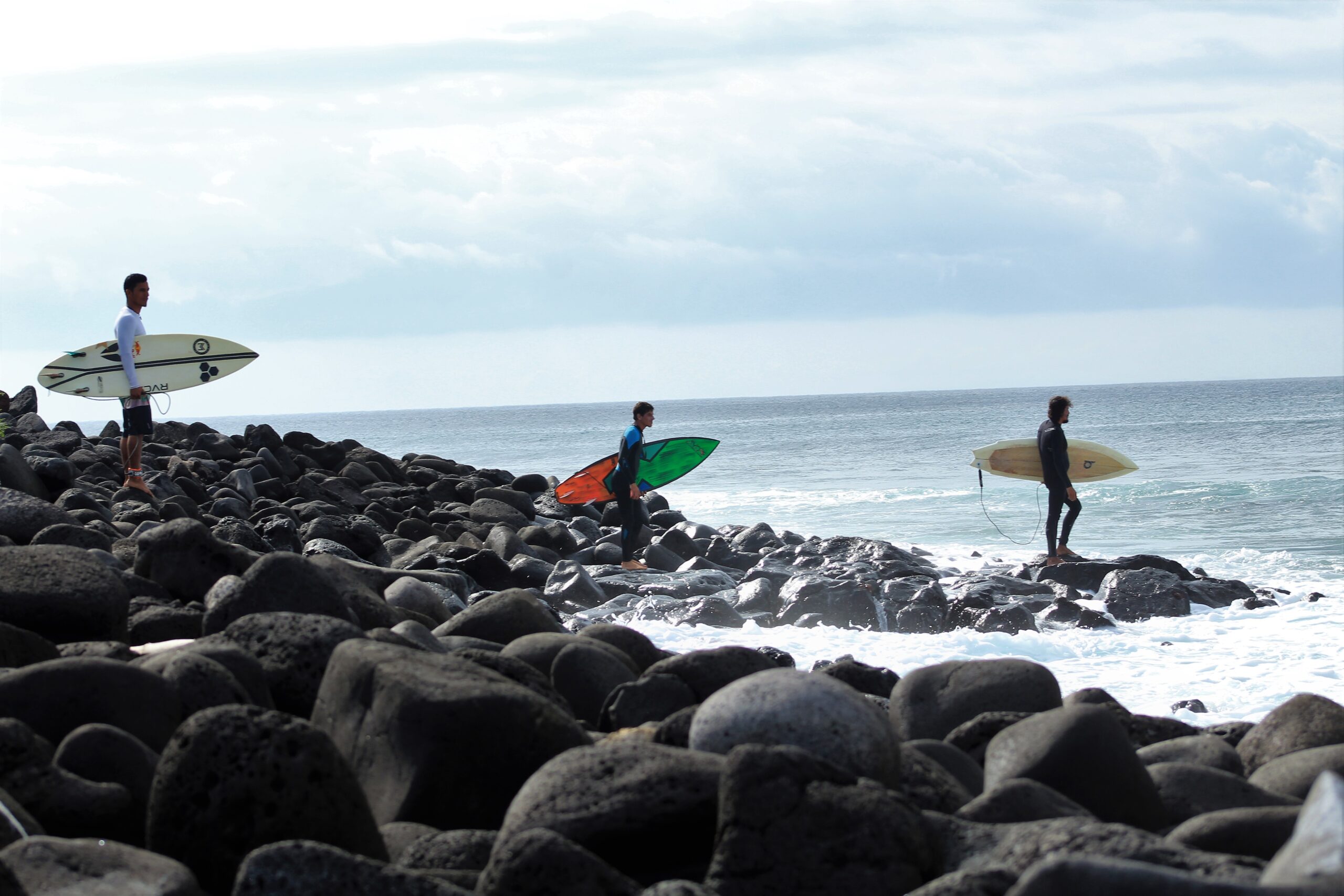three male surfers prepare to enter the water at El Cañon, San Cristobal, Galapagos