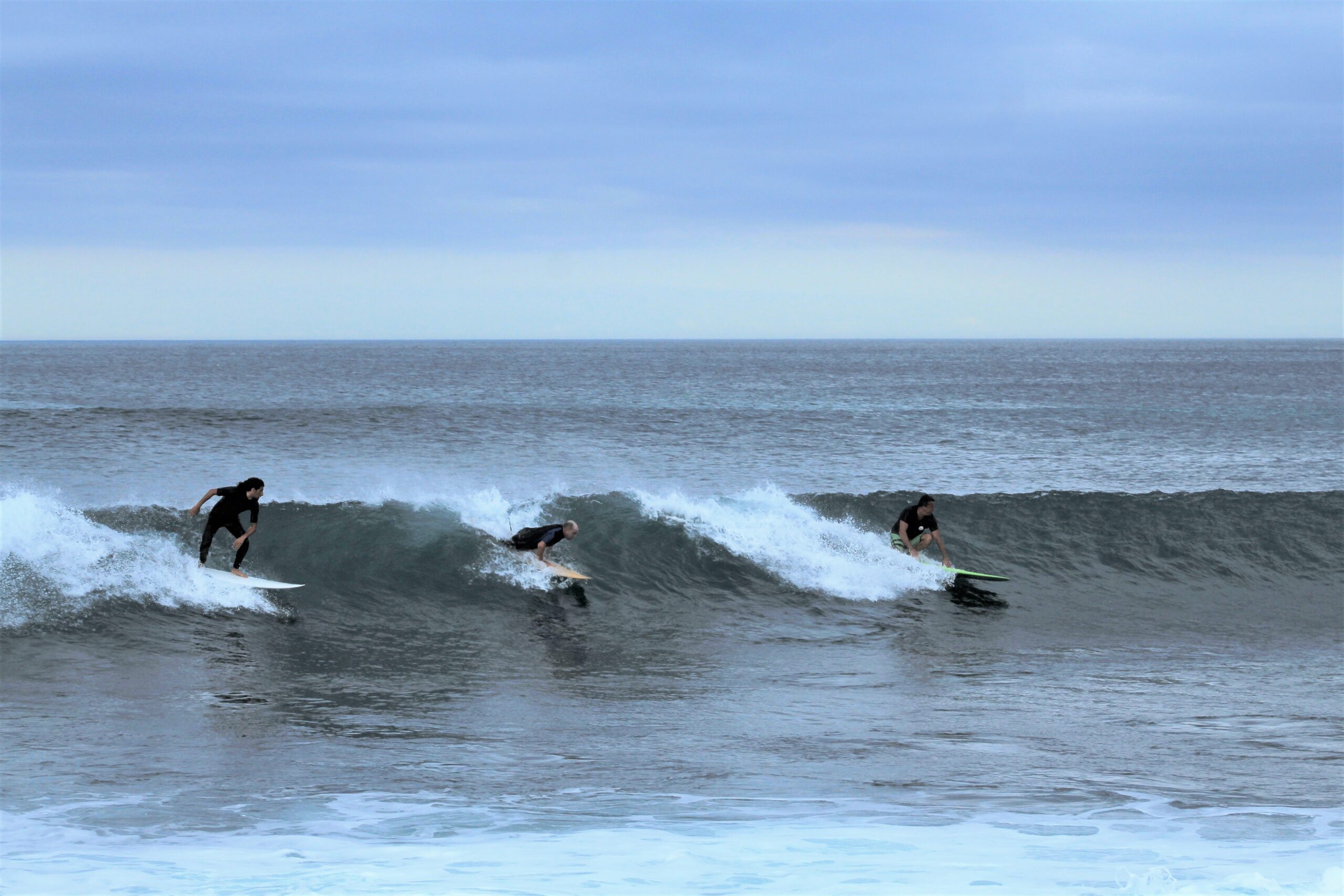 three surfers catch the same wave at El Cañon, San Cristobal, Galapagos