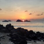 ocean sunset viewed from sandy beach with lava rock and galapagos cruise boats