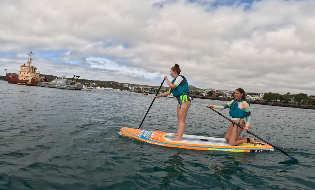 one woman standing and one kneeling on a paddleboard in San Cristobal, Galapagos